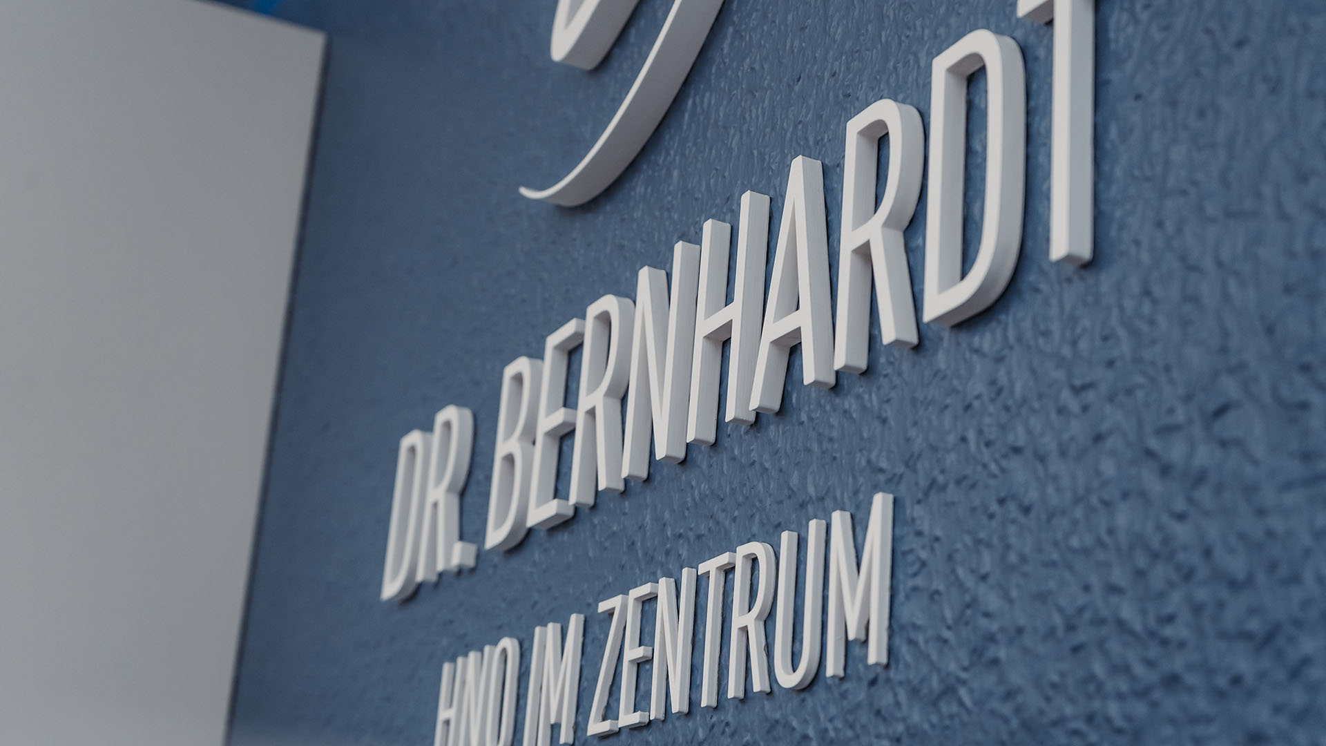 3D-Schriftzug an der Rückwand der Rezeption, der das Logo und die Wortmarke der Praxis darstellt: "Dr. Bernhardt – HNO im Zentrum"