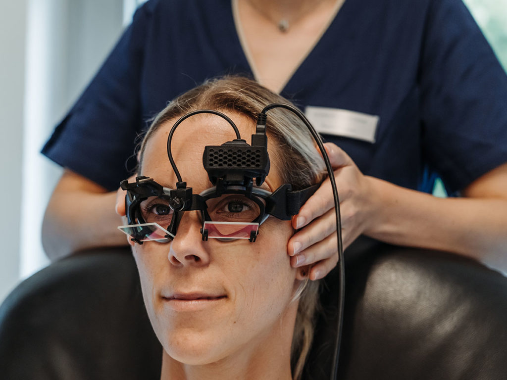 Eine Patientin bei der Schwindeldiagnostik. Eine Mitarbeiterin legt ihr eine Brille für den Video-Kopfimpulstest an.